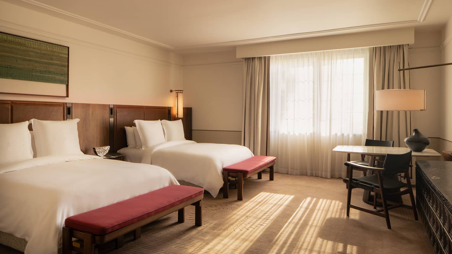 Hotel room featuring two queen beds with red benches at the foot of each