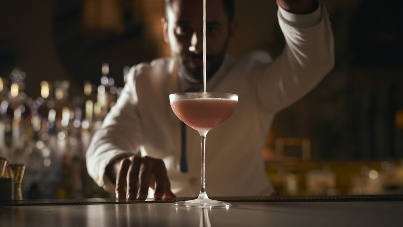 A bartender pours a beverage into a rounded martini glass