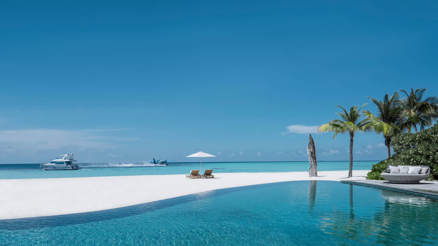 Infinity swimming pool by white sand beach, plane and catamaran boat in lagoon