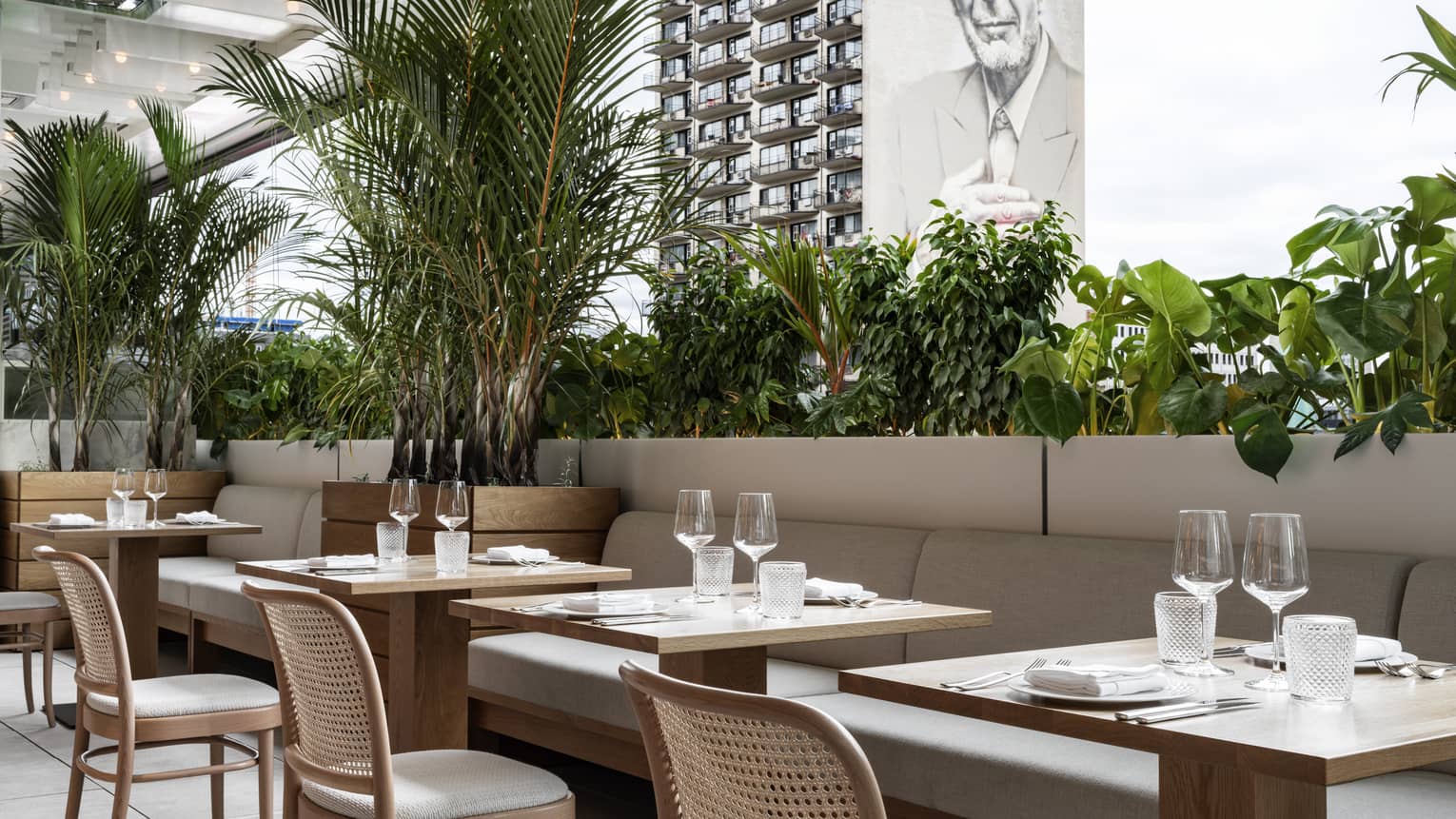 Terrace with banquets, tables set for dinner, greenery, overlooking building with graffitied image of Lennon Cohen