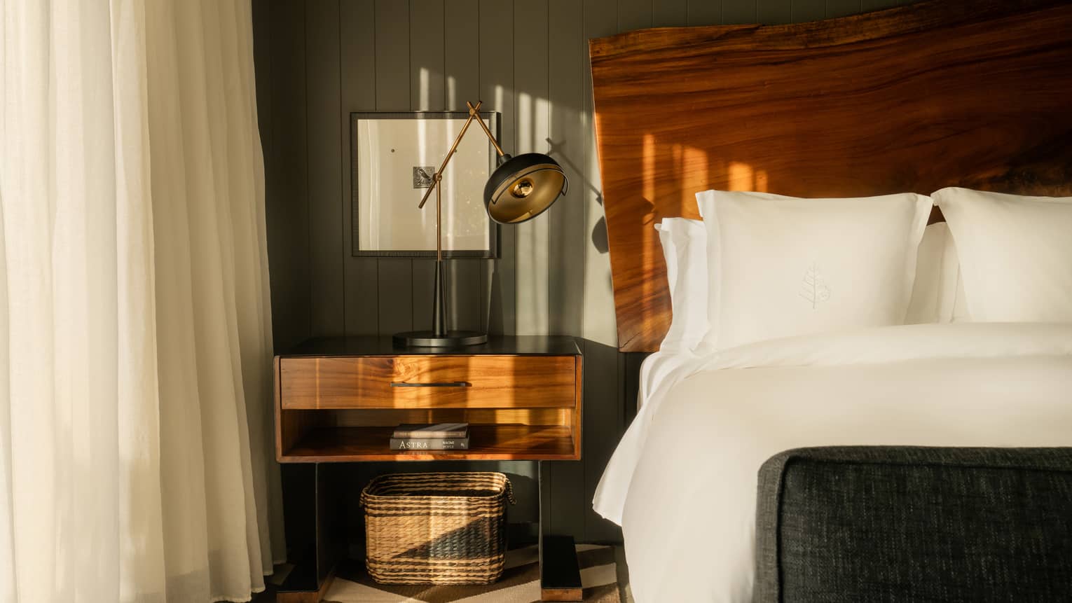 Guest room featuring a king bed with crisp white sheets, and a natural-wood headboard and side table