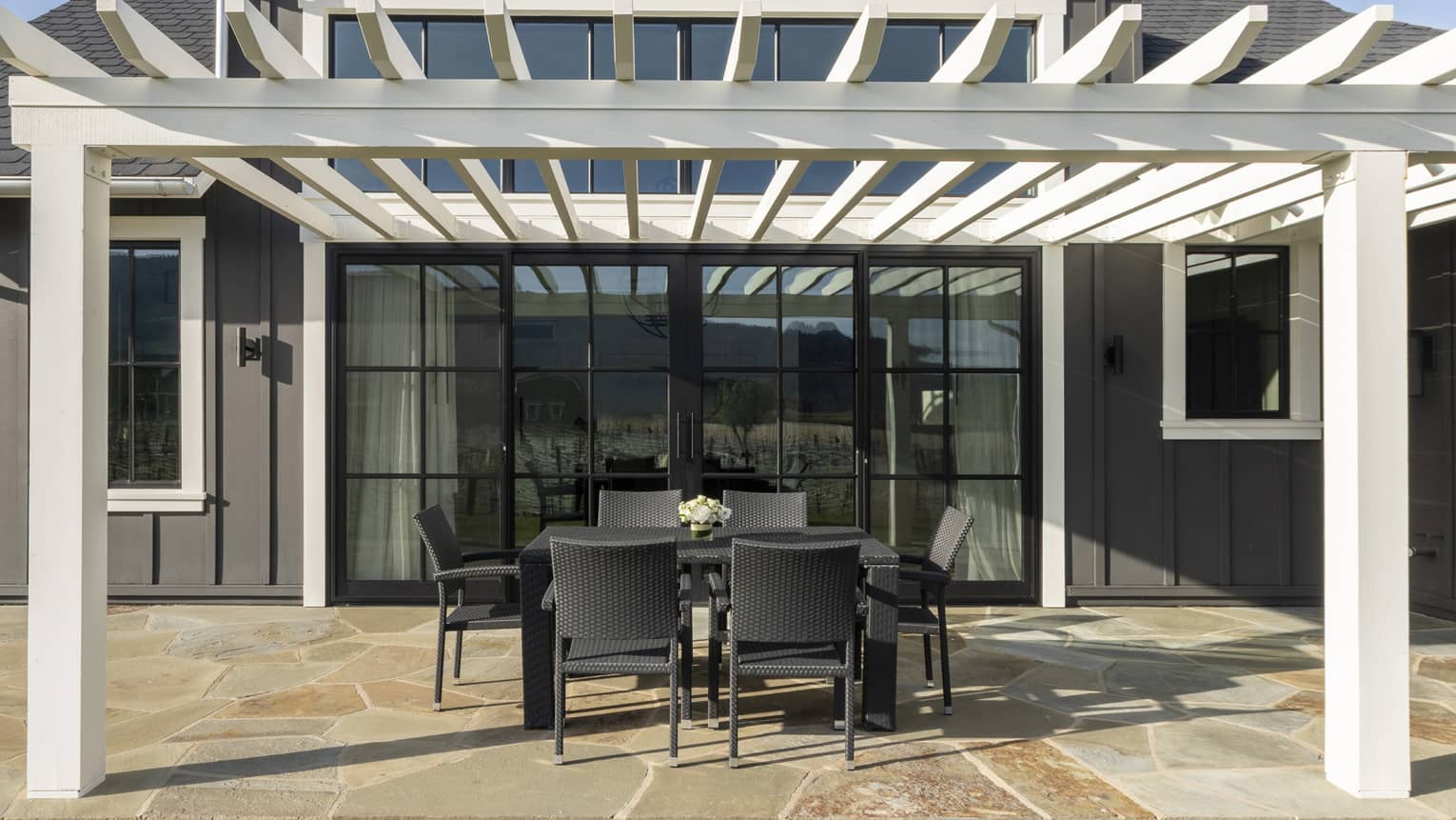 A private villa's stone terrace with dining table under a white pergola