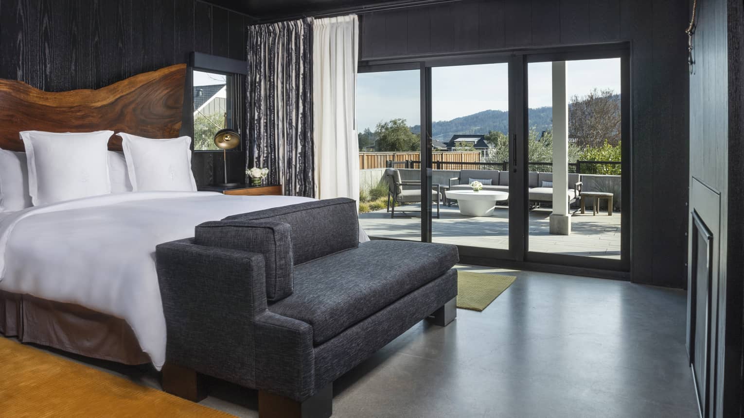 Bedroom with king bed, natural wood headboard, dark grey chaise and walk-out terrace