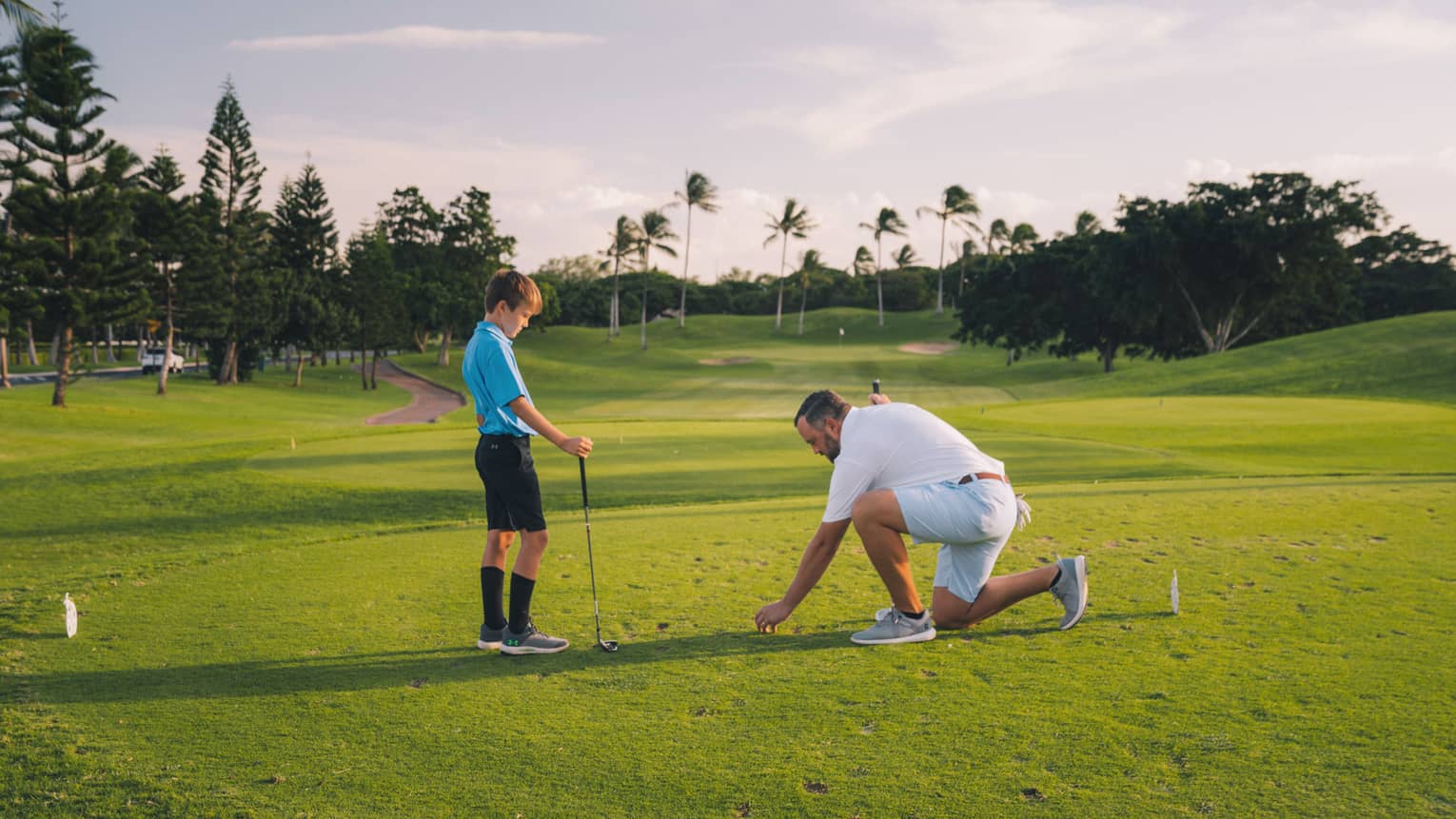 Man and young son play golf on the green, blue sky and palm trees in background