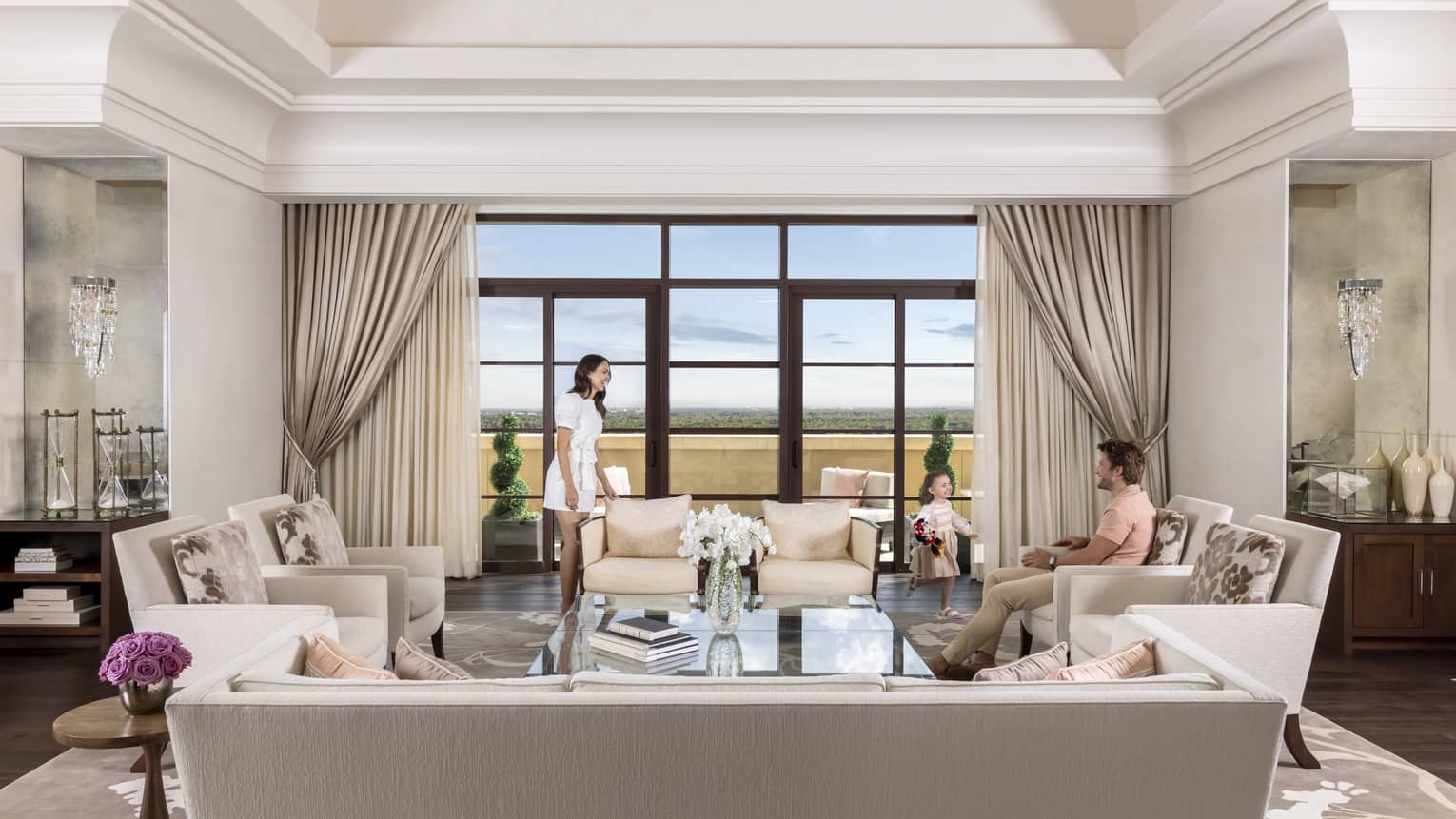 Elegant living room with man, woman and young girl, facing wall of windows