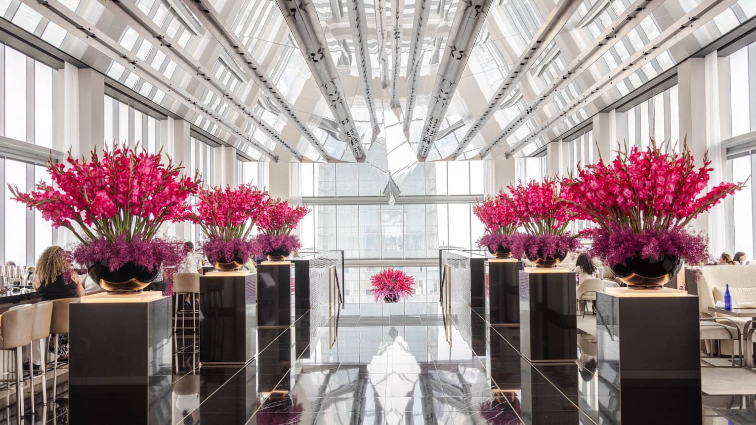An event room with bouquets of pink flowers and windows along the walls and ceiling