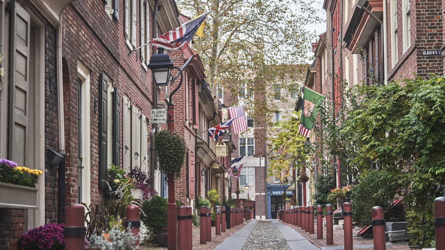 An old cobble-stone street lined with charming brick buildings, plants and patriotic flags