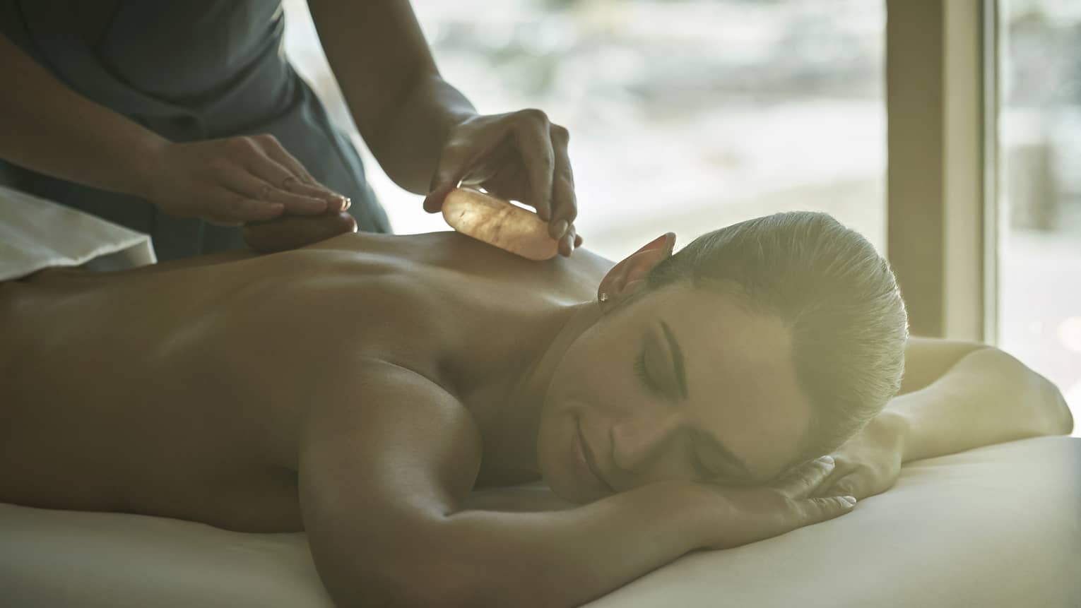 A woman getting a massage on her backs using warm stones.