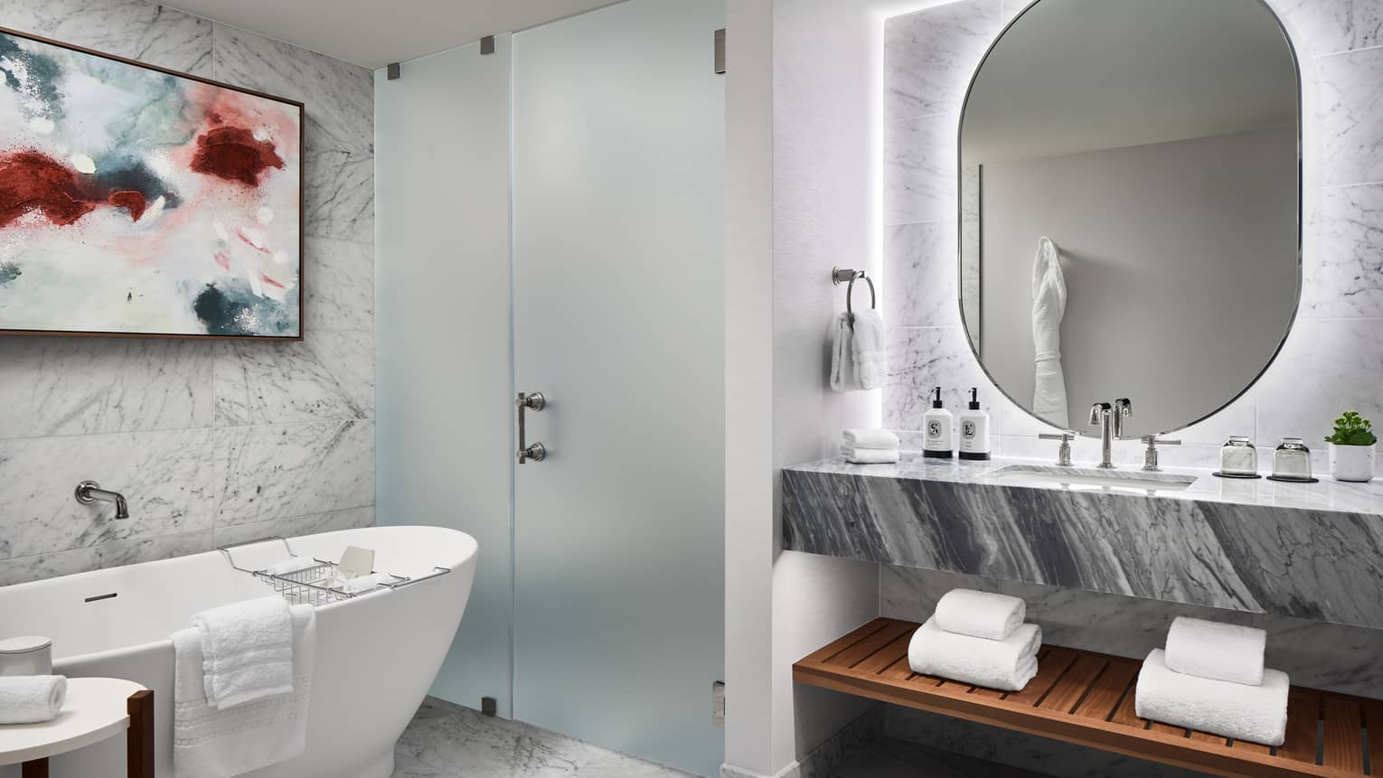 Marble bathroom in a luxury hotel suite, featuring standalone tub, walk-in frosted-glass shower and illuminated vanity mirror
