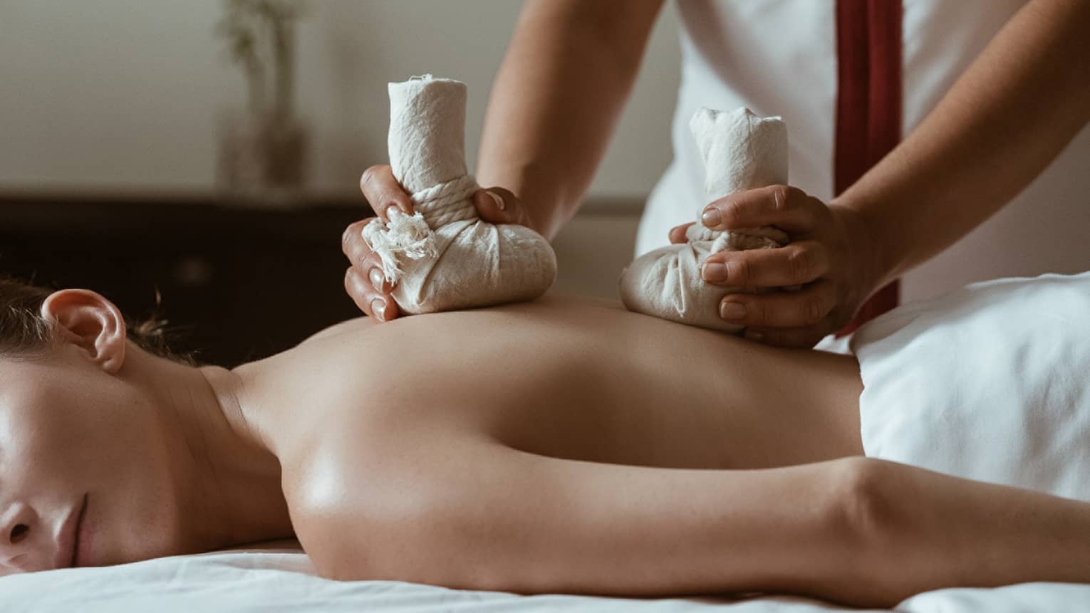 A woman being massaged by heavy stones in cloth bags.