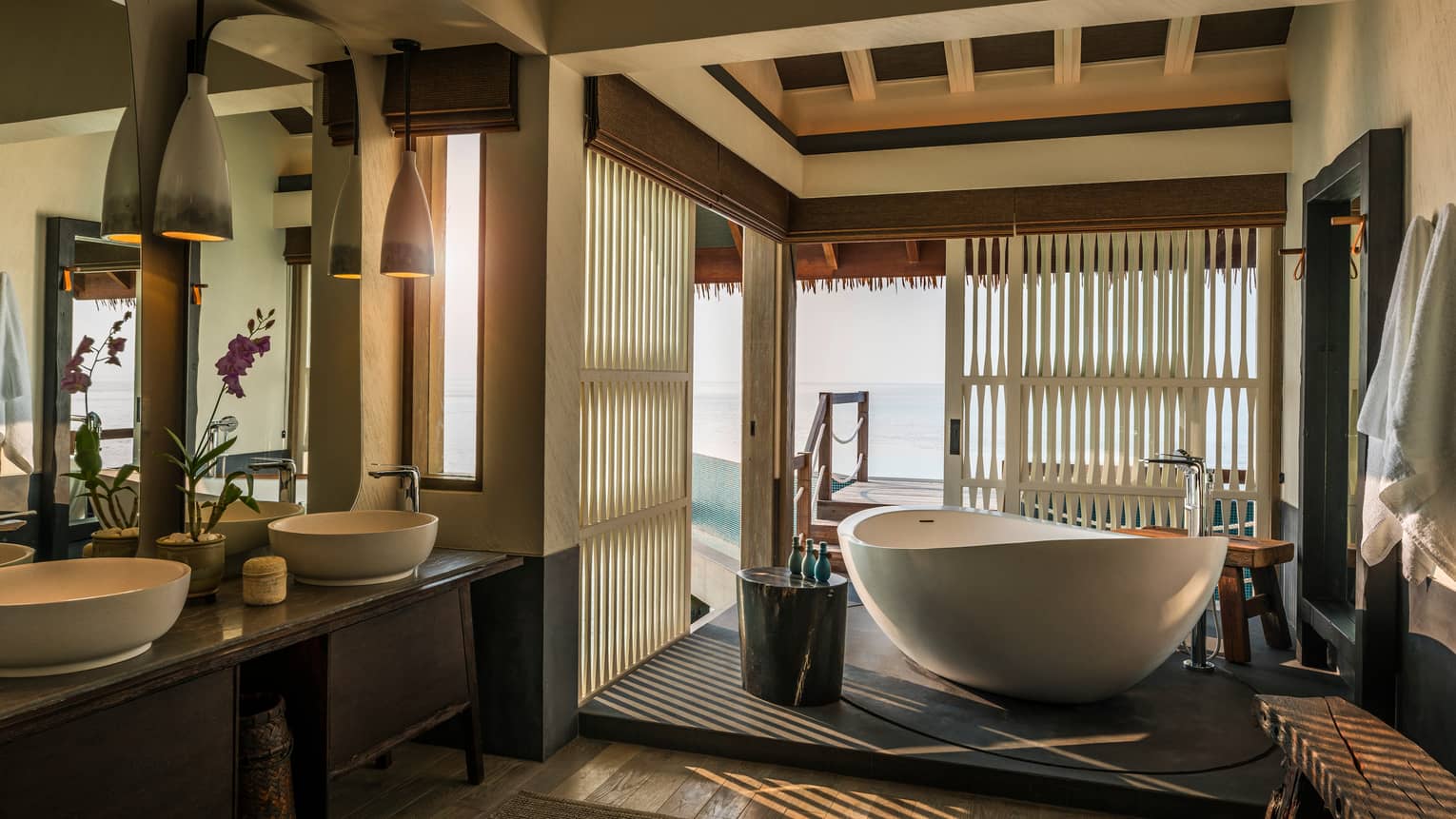 Water Villa bathroom, large freestanding white tub by sliding wood shutters, window, double sinks