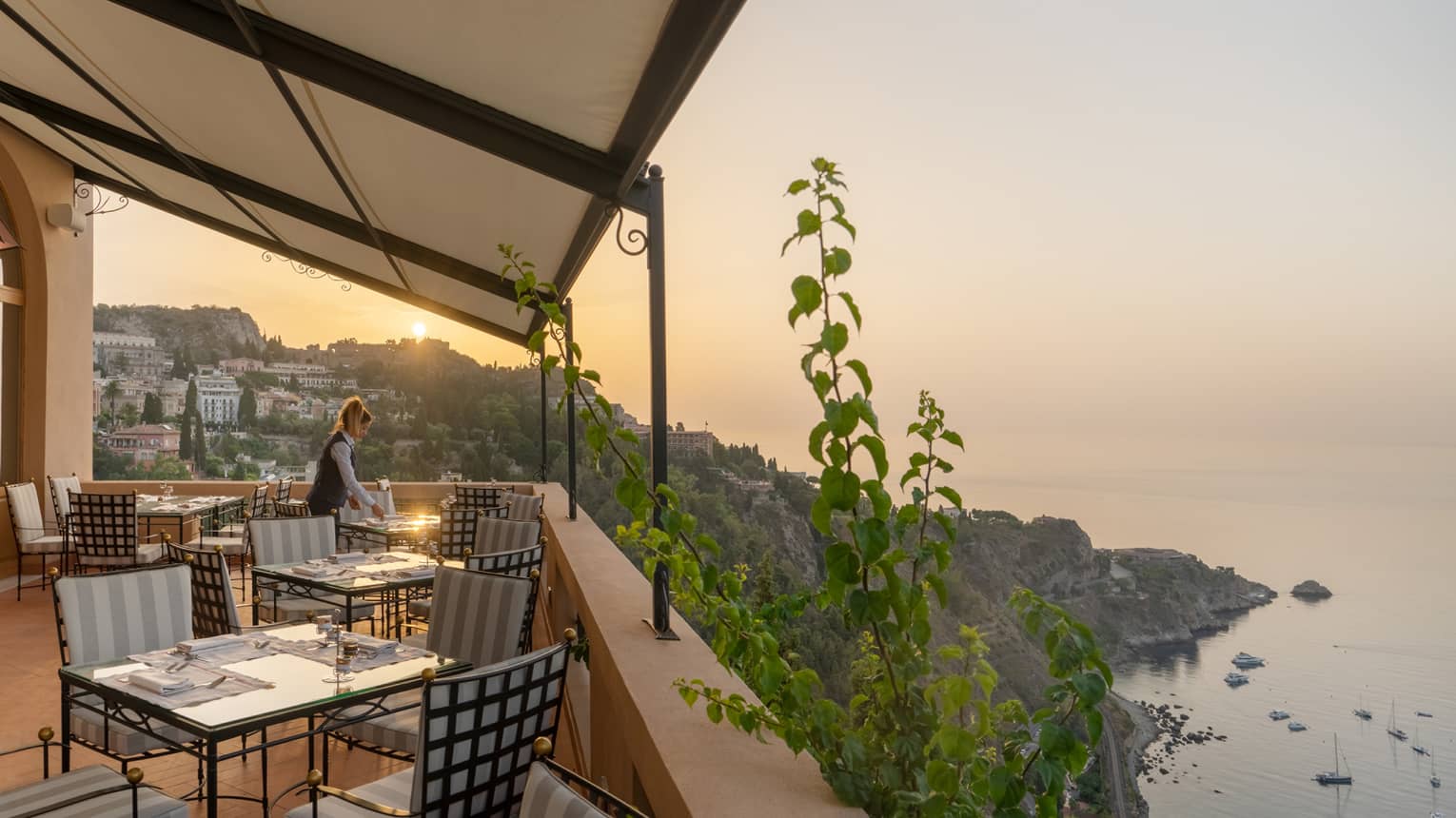 Woman server sets table on restaurant terrace overlooking the sea
