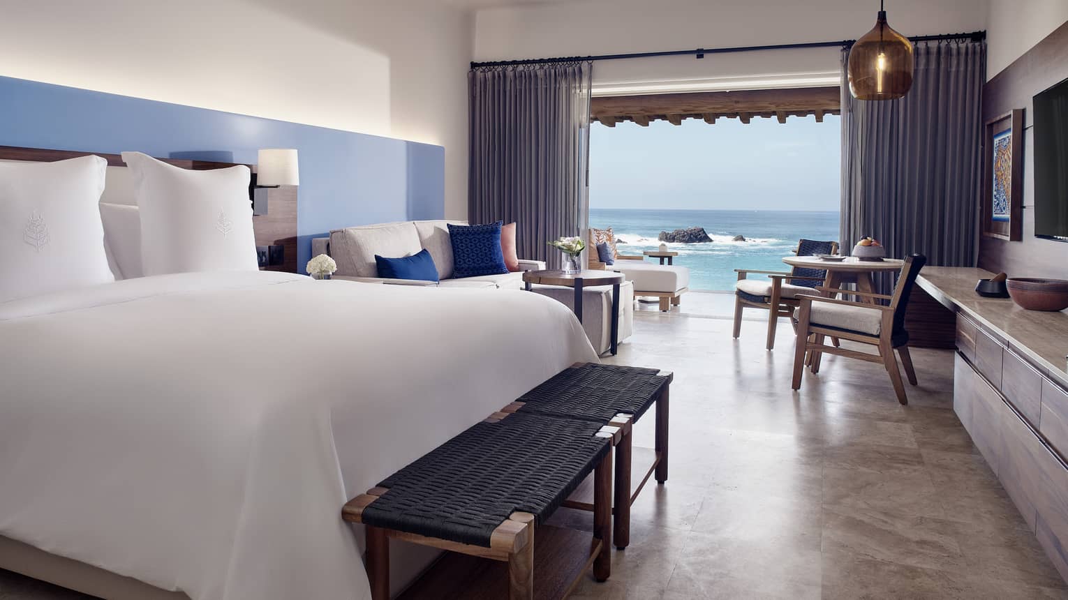 A hotel room with a bed, large window, chairs, and a sofa.