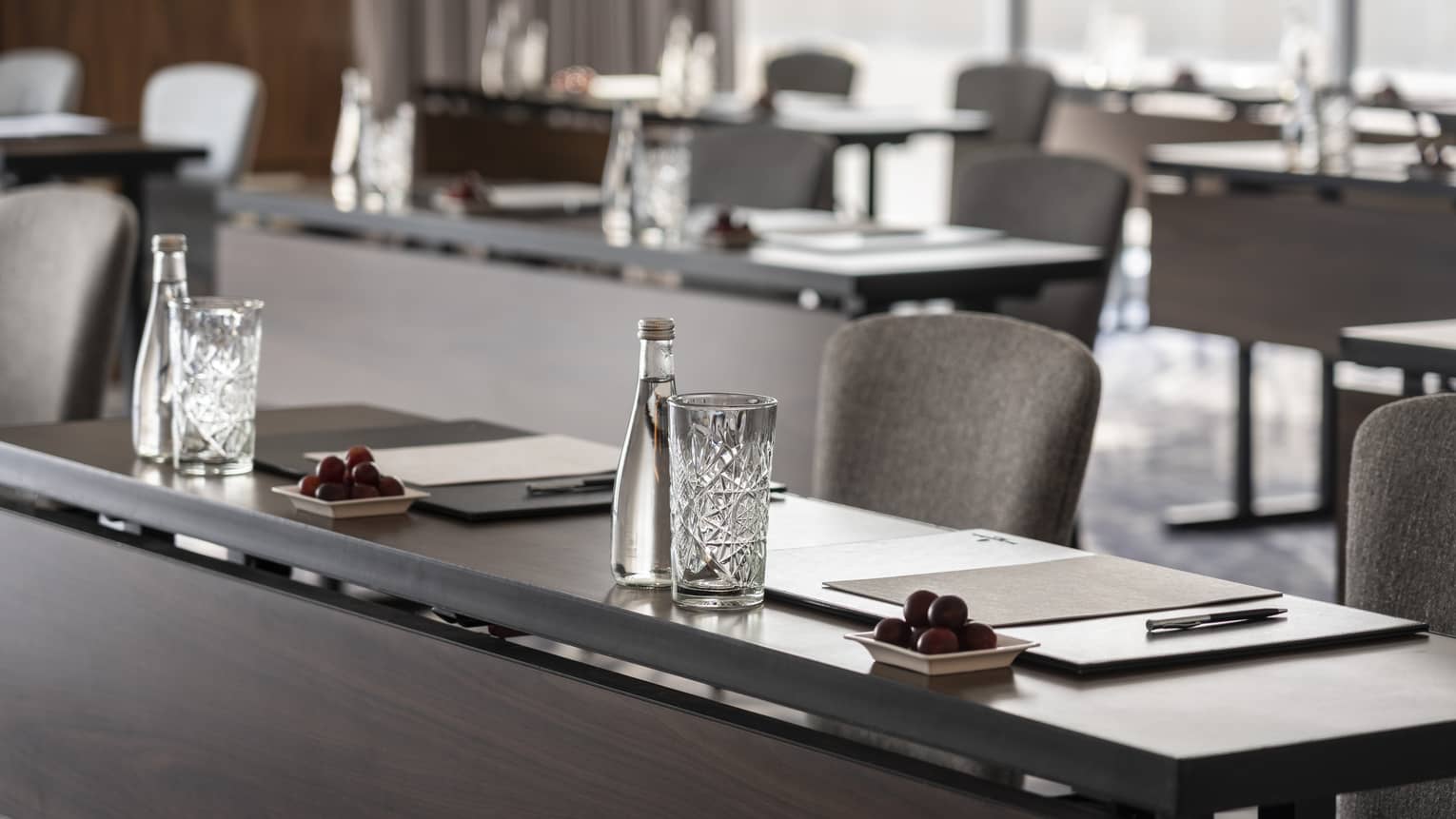 A close up of long desks with papers and water placed at each seat.