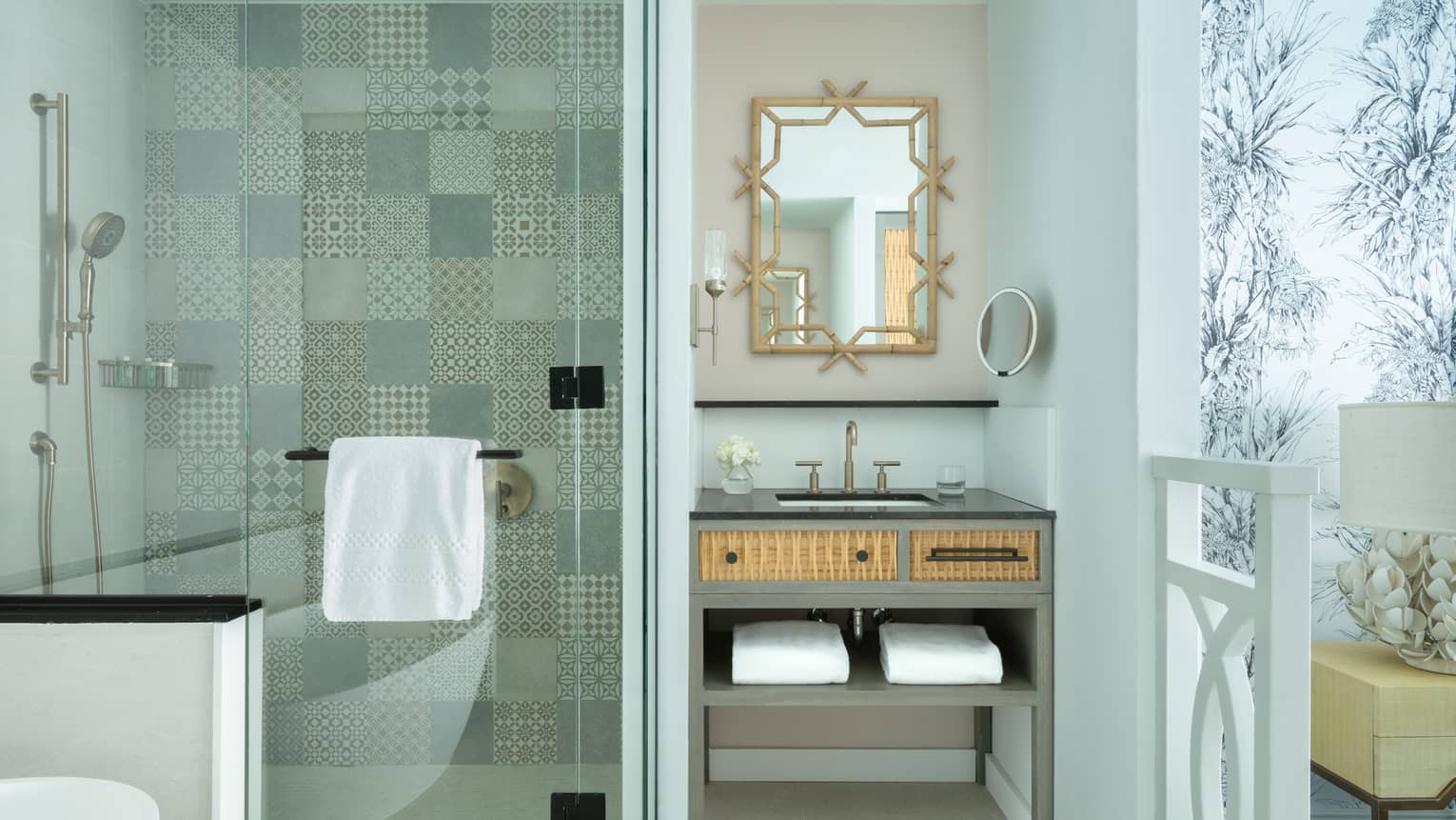 Luxury resort bathroom with a patterned tile shower, ornate vanity mirror and wicker-accented sink cabinet