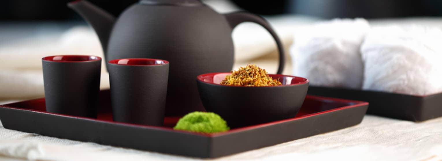Black-and-red modern teapot with two mugs and bowl of loose-leaf chamomile on serving tray