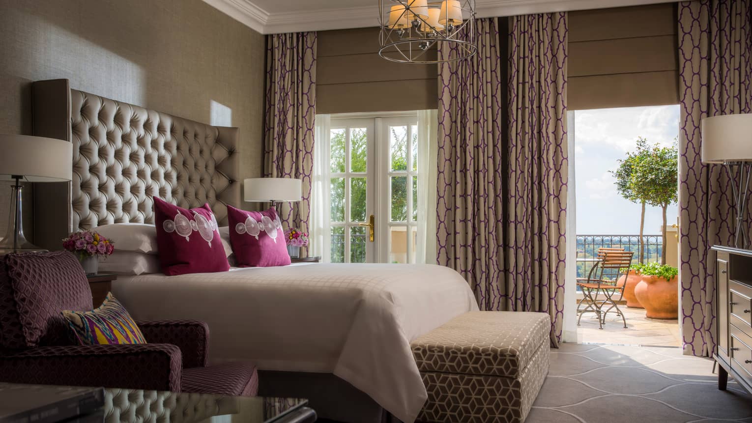 Presidential Suite bed against tall padded headboard, armchair and padded bench, large picture windows with patterned curtains