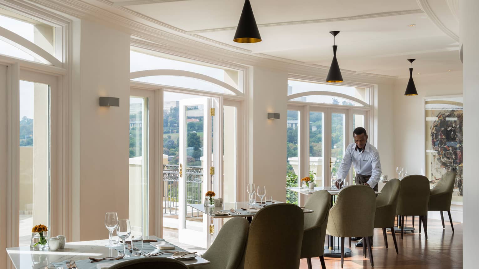 Waiter sets dining table in sunny Flames restaurant dining room