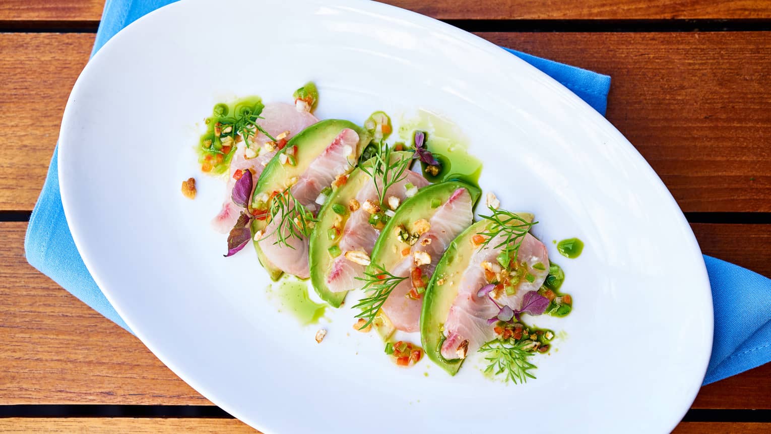 Kanpachi Crudo sliced fish arranged with avocado, toasted corn, greens