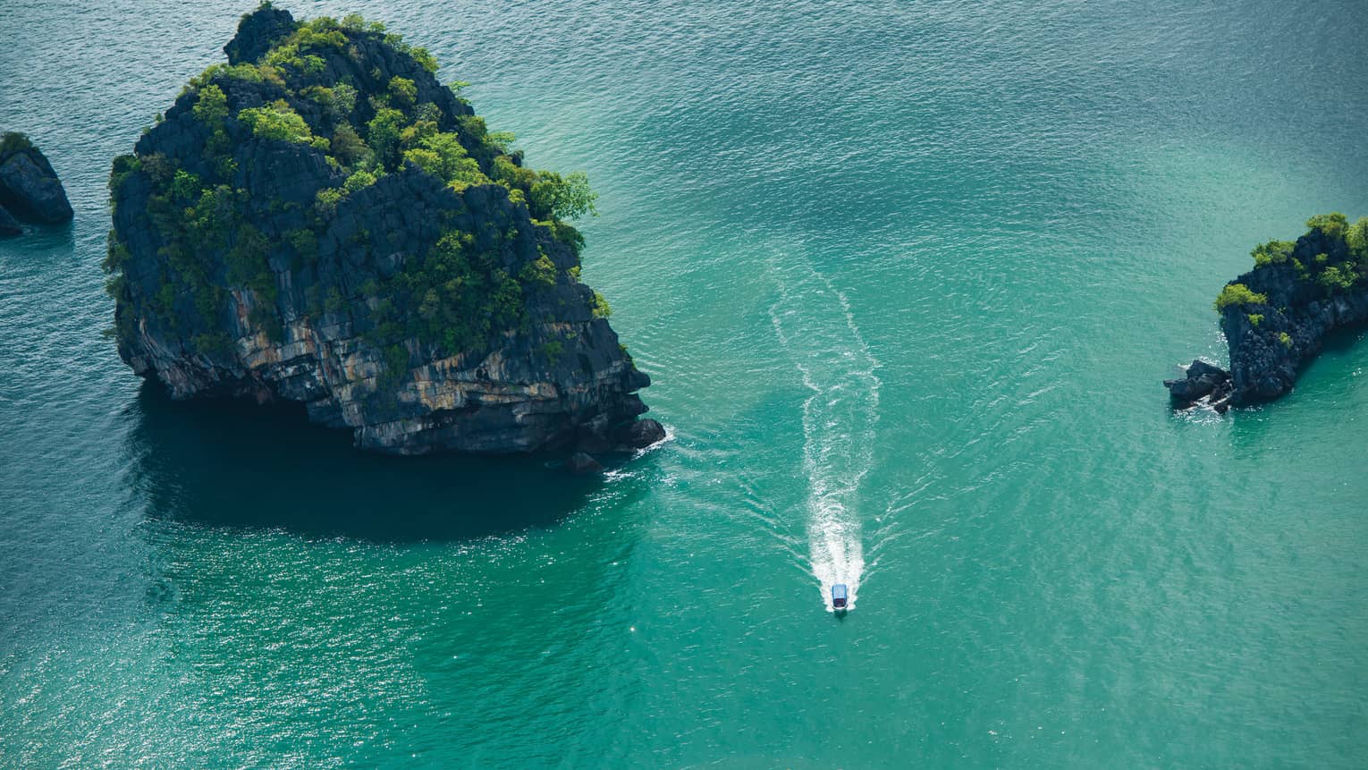 Ariel view of a boat driving through rock structures on emerald green water