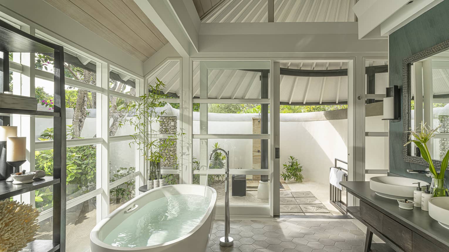 Luxury bathroom with walls of windows and standalone tub, opening to outdoor shower and garden at tropical resort