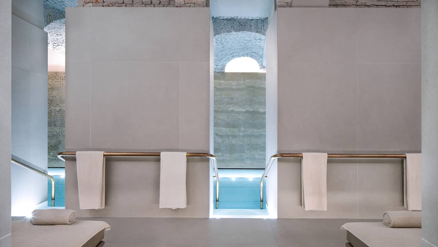 Concrete spa pool deck with white spa loungers, white towels hanging and pool entry between tall white walls