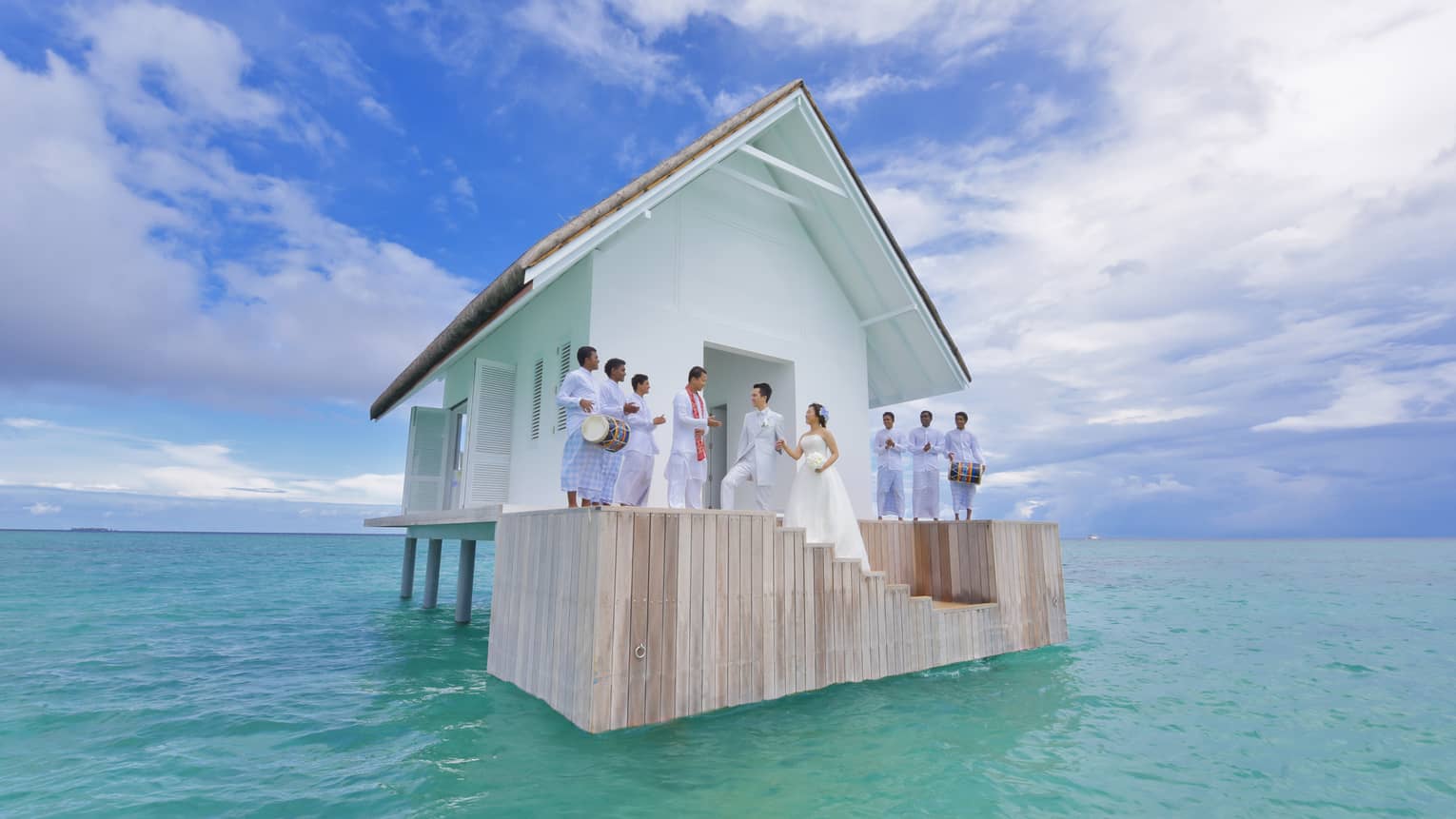 Wedding ceremony on steps of small white bungalow in middle of blue lagoon