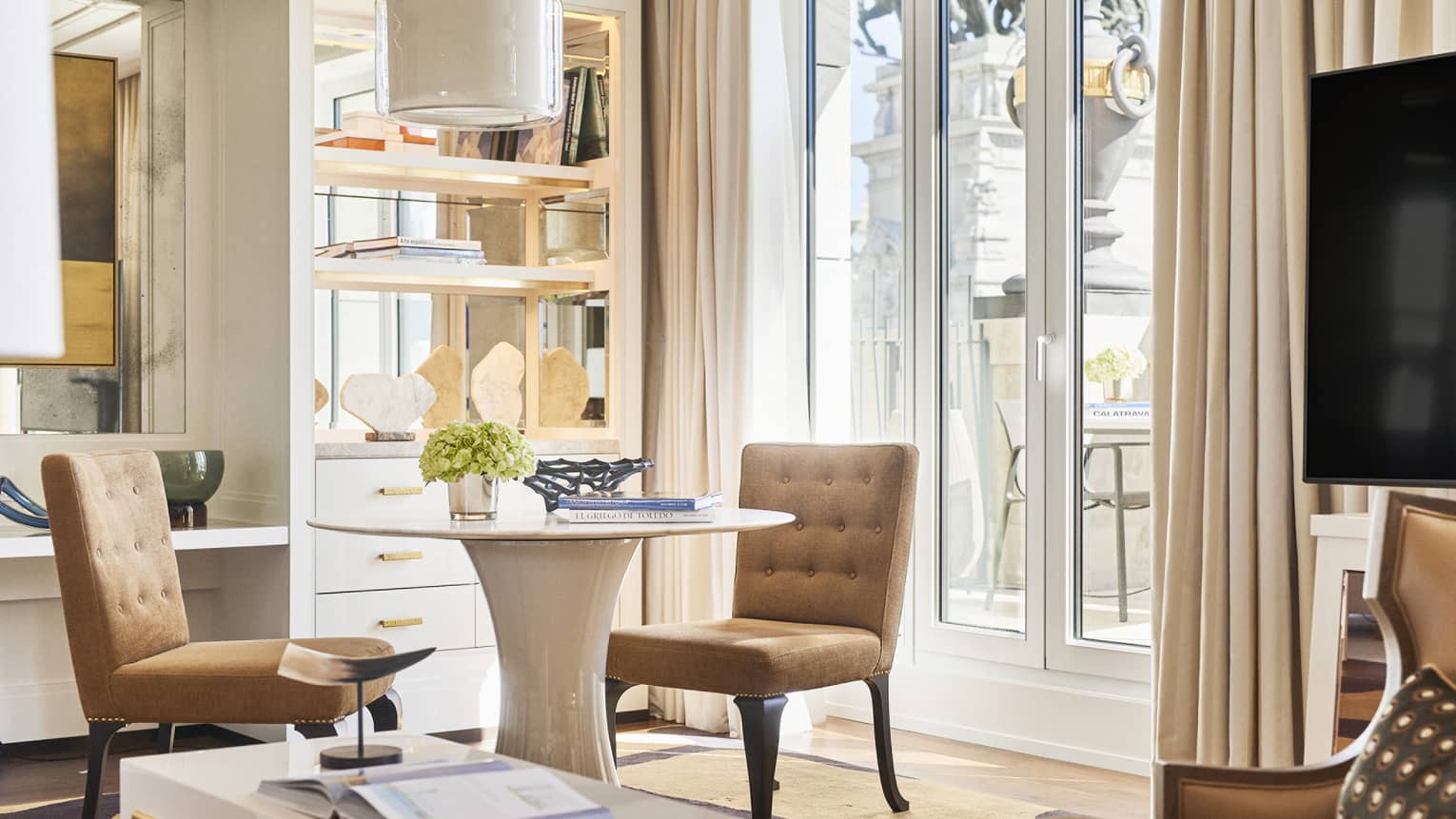 Round table and two light brown chairs, built-in shelving, glass doors 