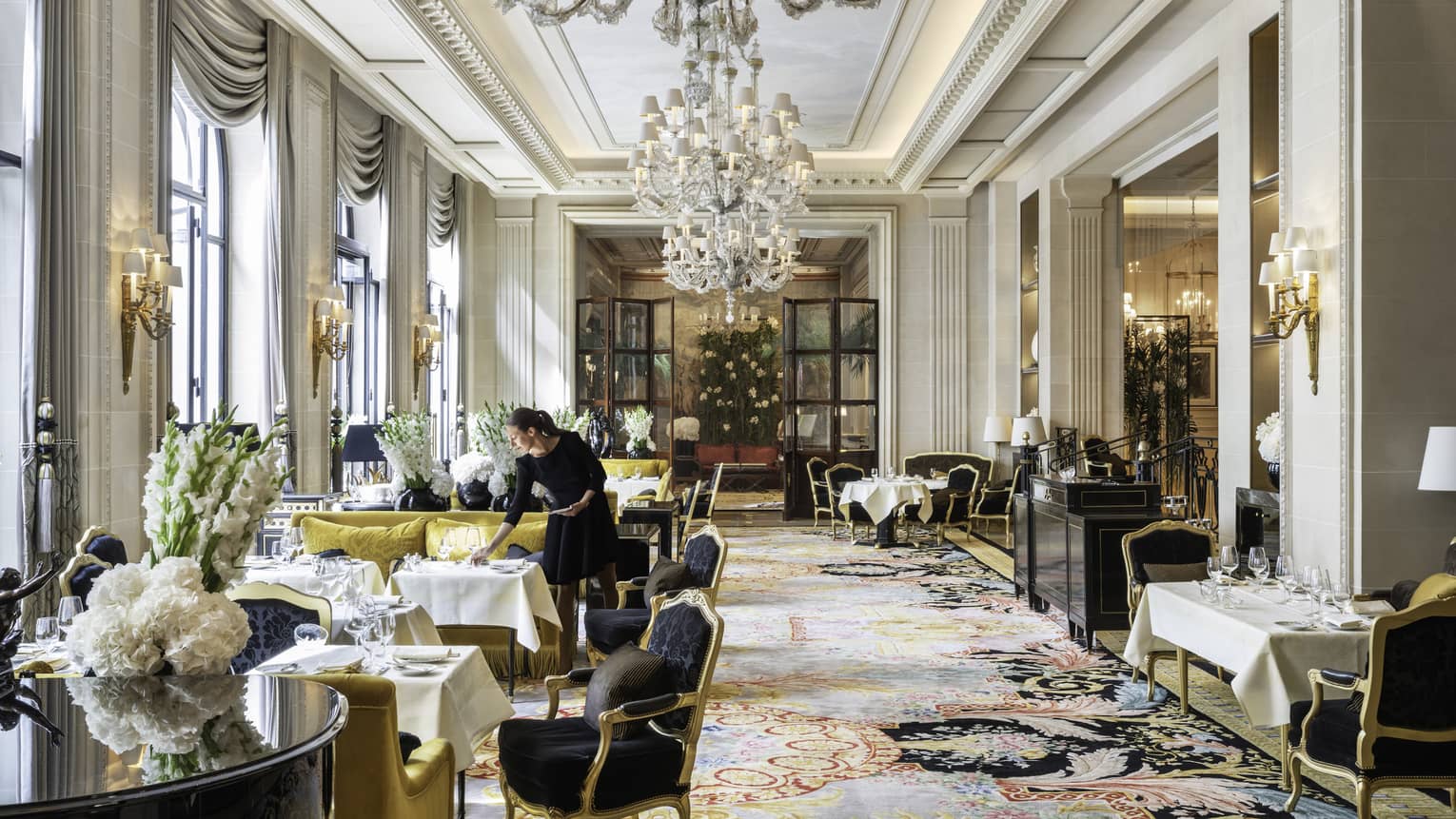 Staff member setting table in formal dining area with Queen Anne chairs, chartreuse sofas, white floral arrangements and floor-to-ceiling windows
