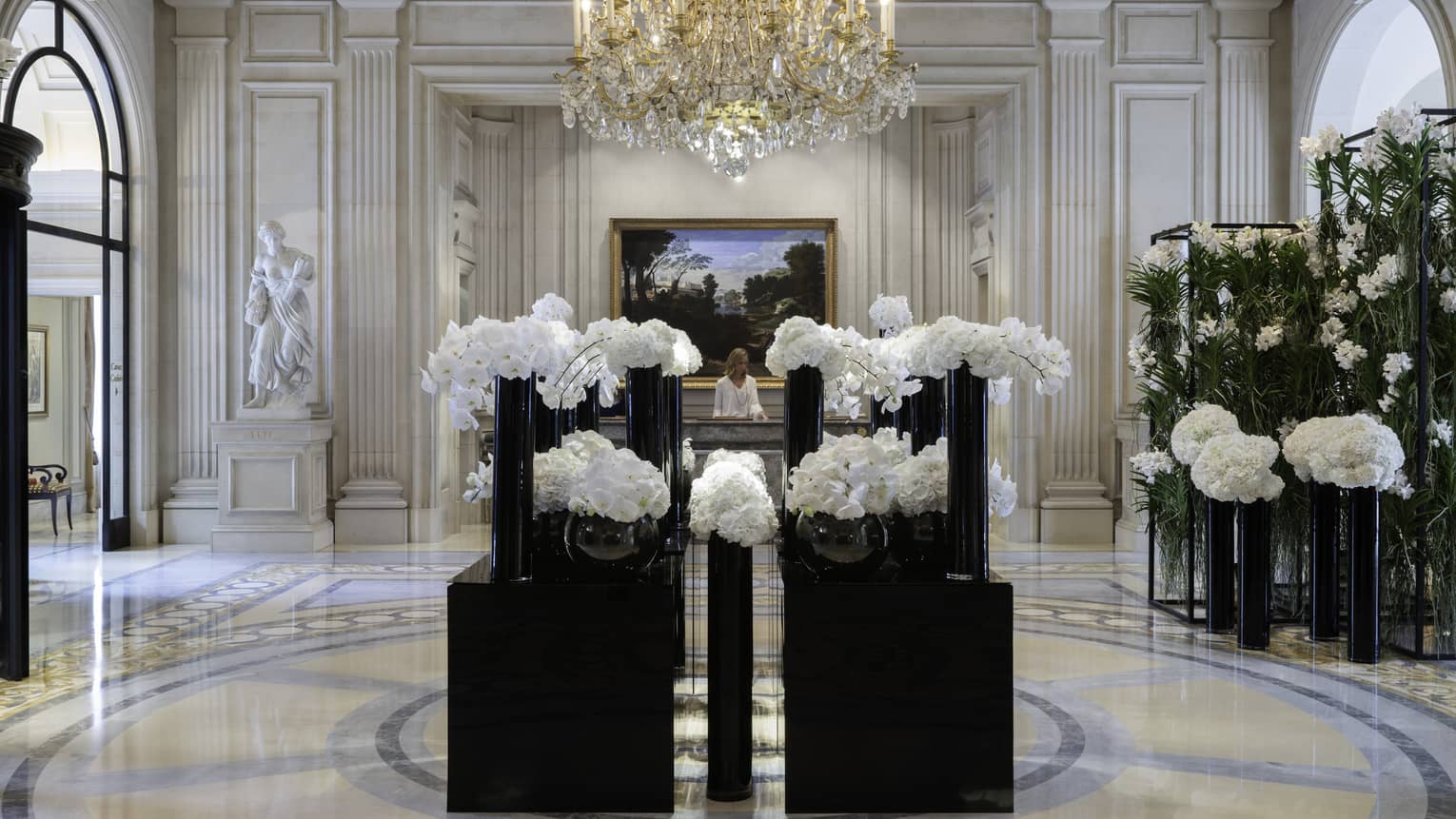 Elegant hotel lobby with marble floors, tall black vases and white flowers under crystal chandelier