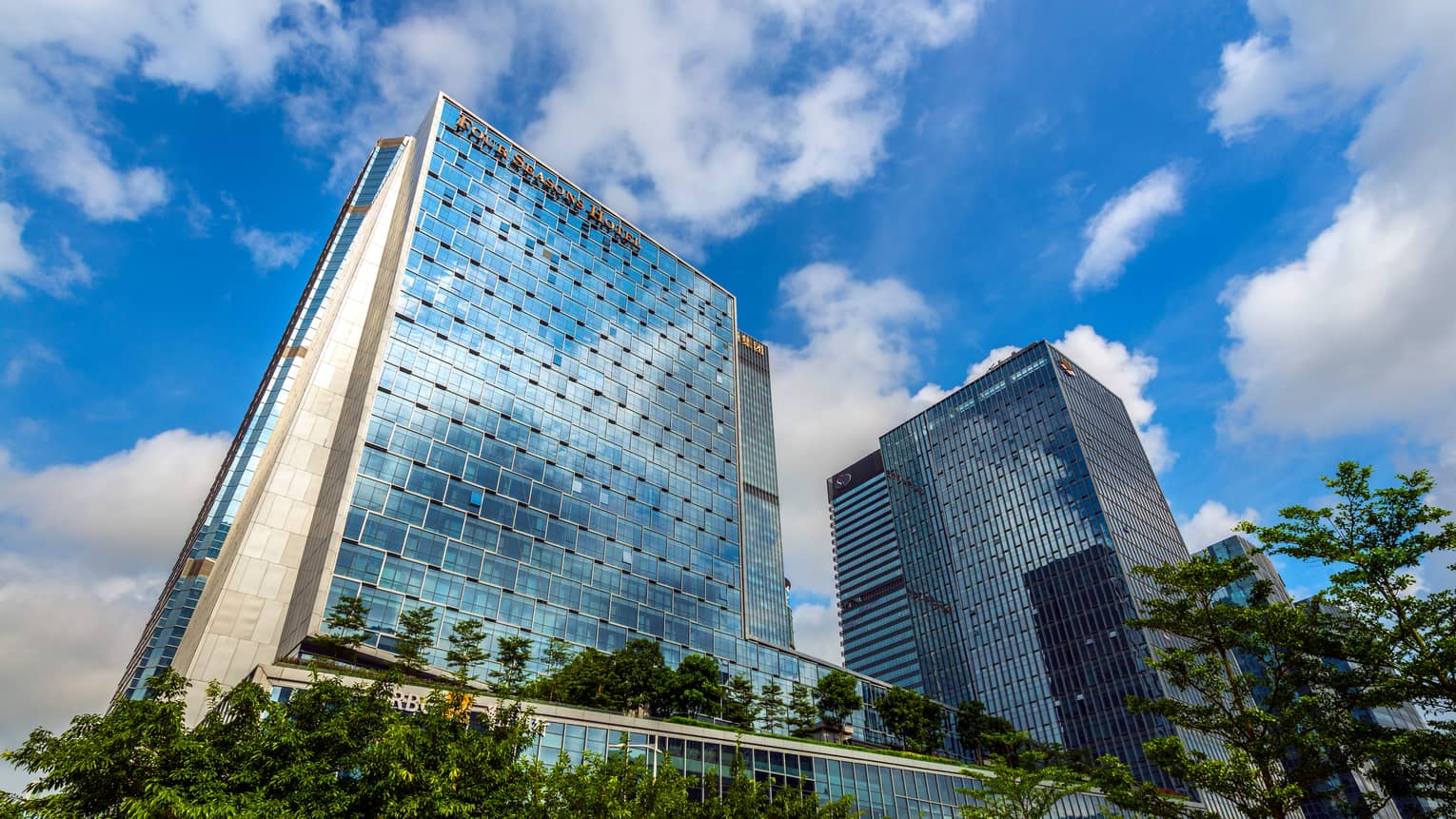 Looking up at Four Seasons Hotel Shenzhen glass towers against blue sky