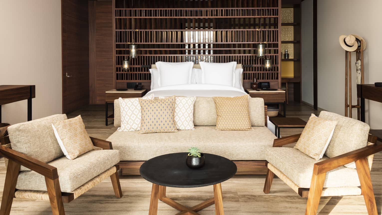 A stylish hotel bedroom with a neutral color palette, featuring a comfortable bed, a cozy seating area with beige cushions and wooden accents, creating a warm and inviting atmosphere