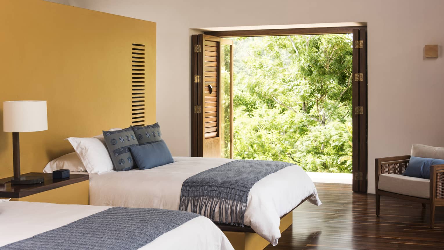 Bedroom with two double beds, wooden floors, and walk-out terrace with trees