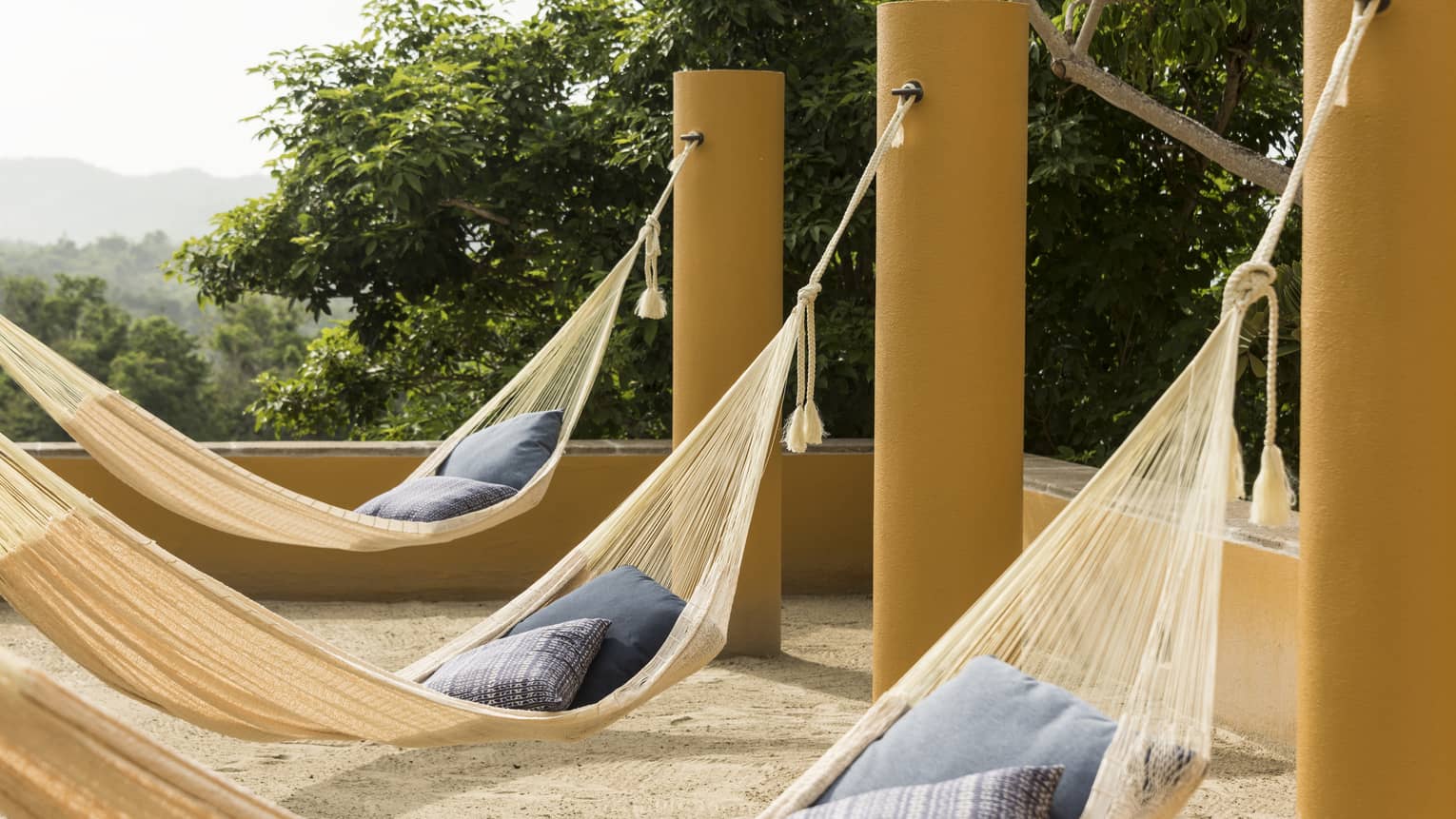 Three hammocks hanging with pillows on outdoor ocean-view terrace