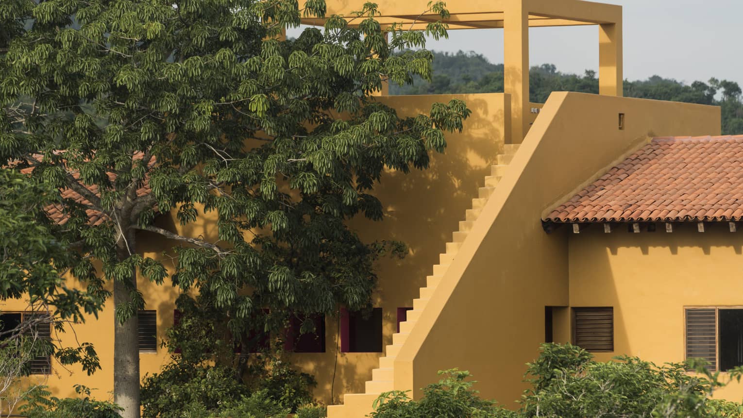 Exterior of villa with yellow stucco walls and lush trees