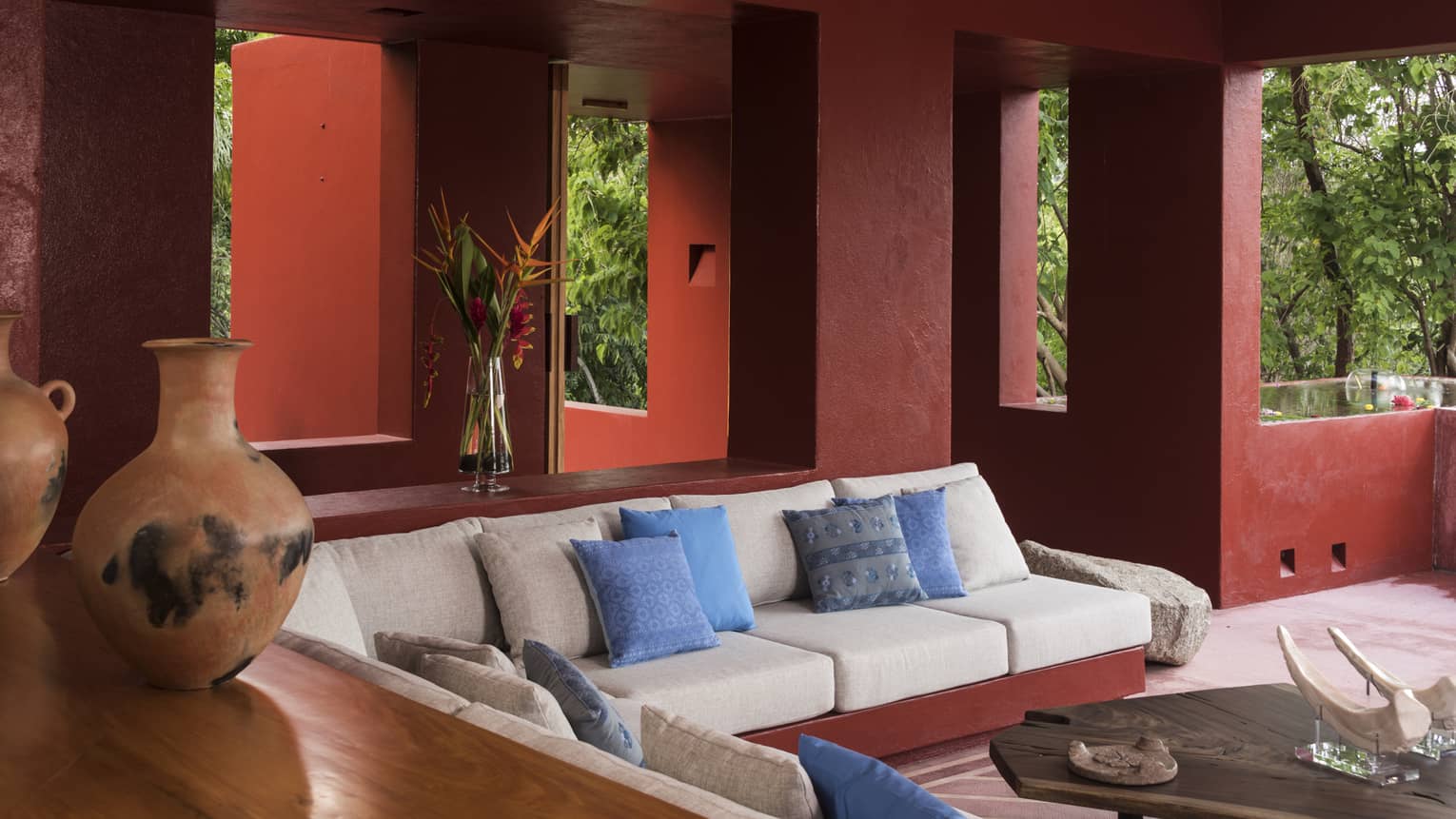 Living room with red walls and windowless openings to lush jungle forest