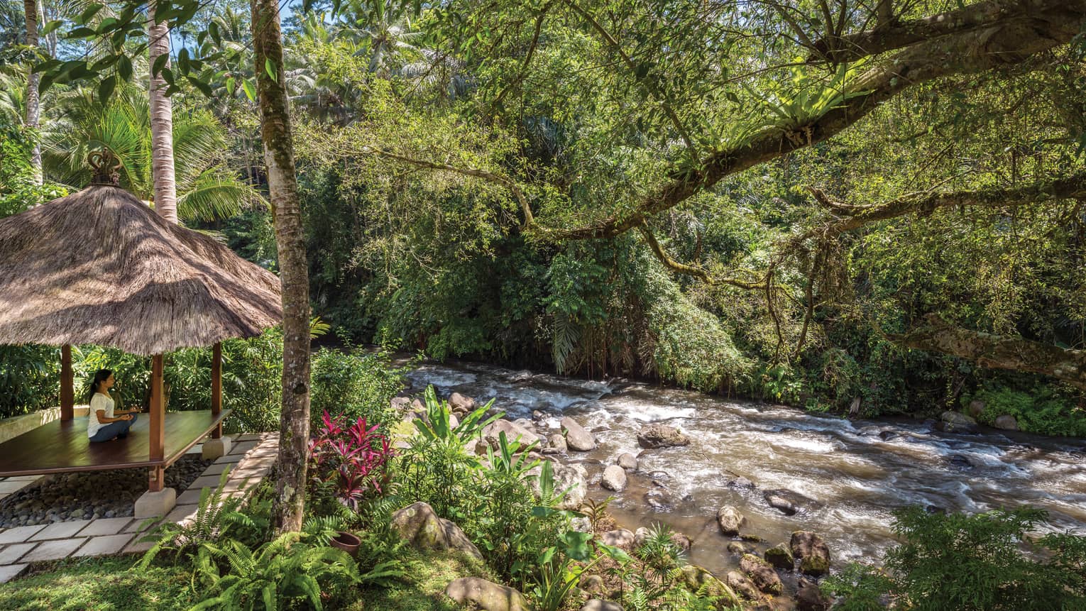 A guest meditating in a pavilion next to a flowing river in Bali