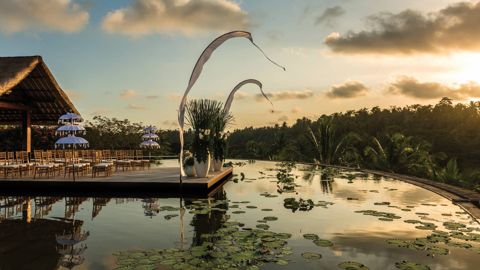 Rows of chairs set up for wedding ceremony on patio over lotus pond at sunset