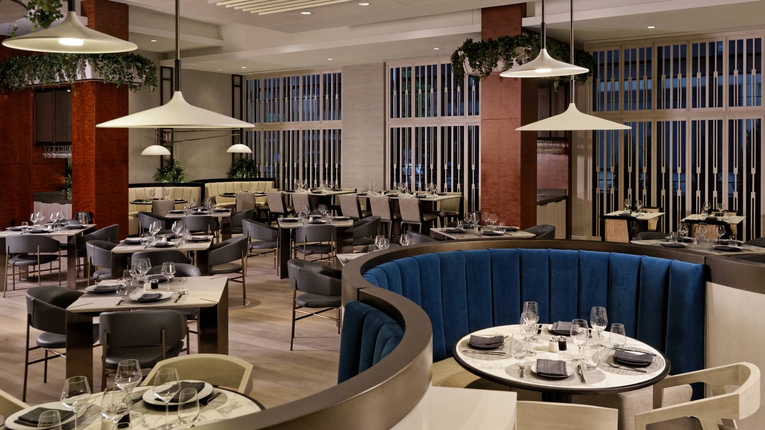 A restaurant with a variety of tables from square to round booths, white lamps hang from the ceiling.