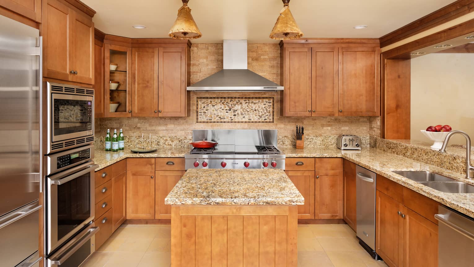 Kitchen with granite countertops, stainless steel appliances, wood cabinets, an island and a decorative stone backsplash under the range hood