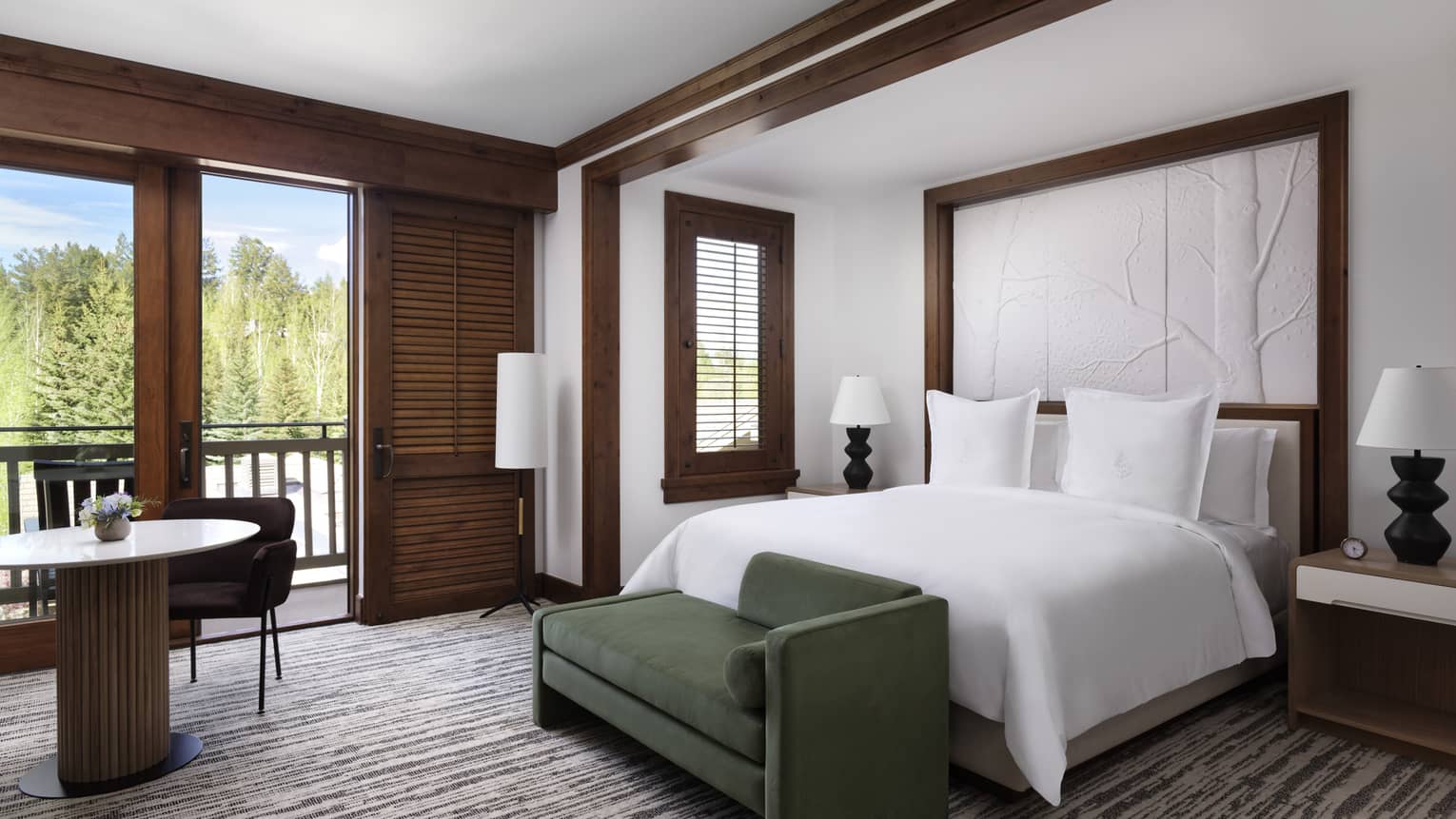 Hotel room with king bed, dark green chaise, small table with two chairs and balcony