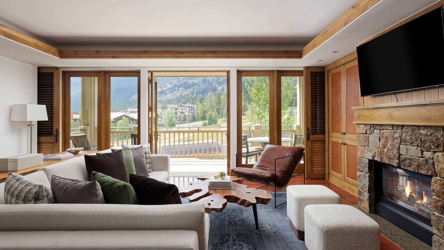 Living room with sofa, leather chair, two stools, stone fireplace and TV, with walk-out balcony