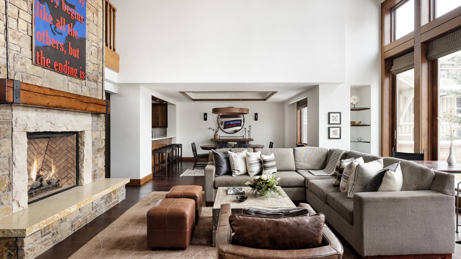 Luxury living room with a stone fireplace, statement art piece, sectional sofa, leather armchair and ottomans, and views of a dining area and bar seating