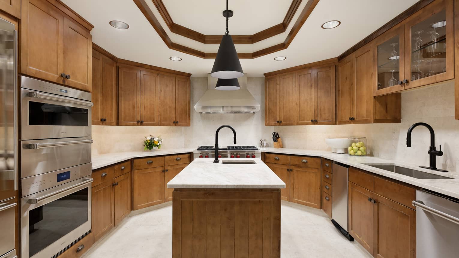 Luxury kitchen with wood cabinets, stainless steel appliances, marble countertops, an island with a black faucet and pendant lighting overhead