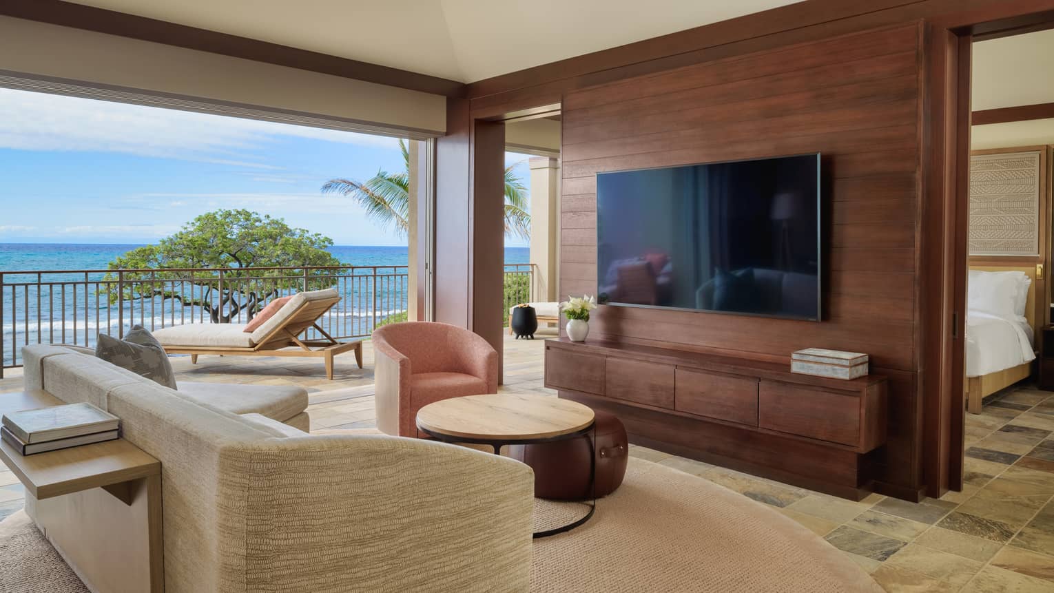 Living area separated from bedroom by a dark wooden wall with mounted TV, opening to private lanai with ocean views