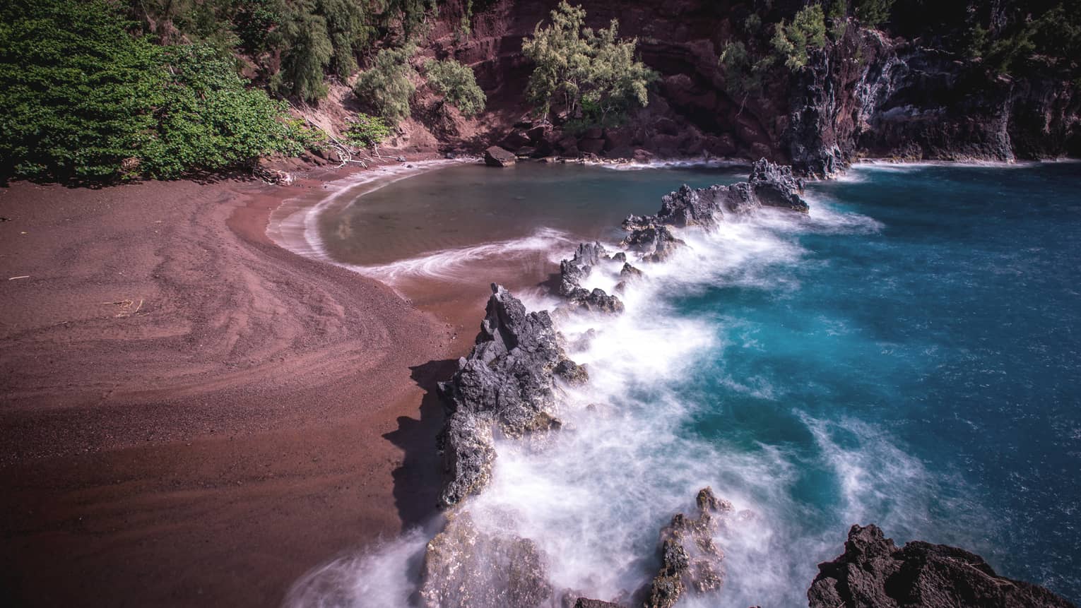 A red sand beach with waves crashing onto the sand.
