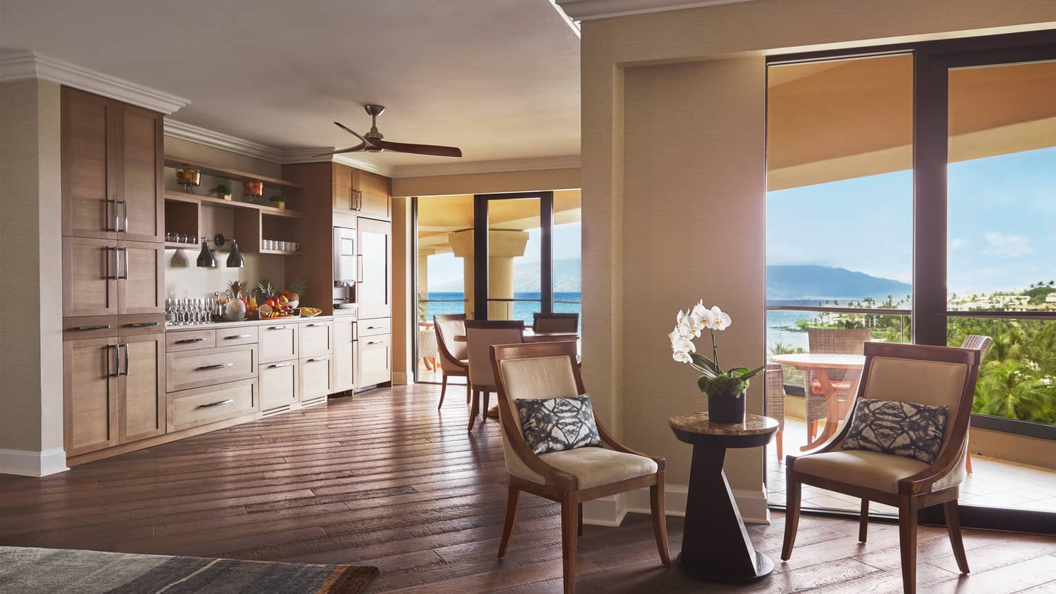 Open-concept suite with kitchenette, seating area and ocean-view balcony under natural light
