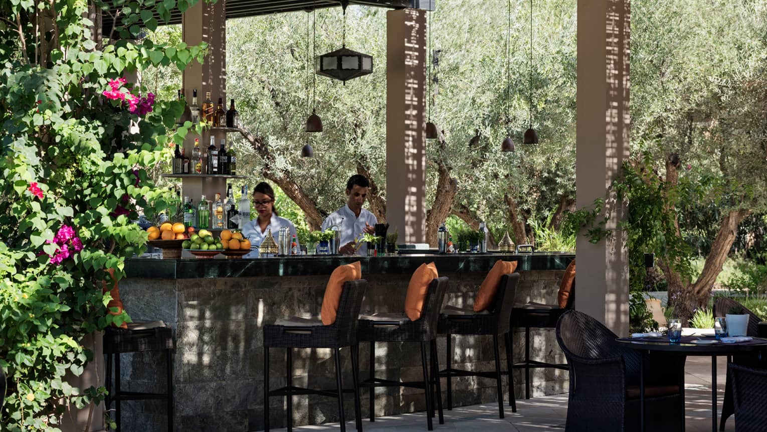Bartenders mix cocktails at small outdoor bar on garden patio