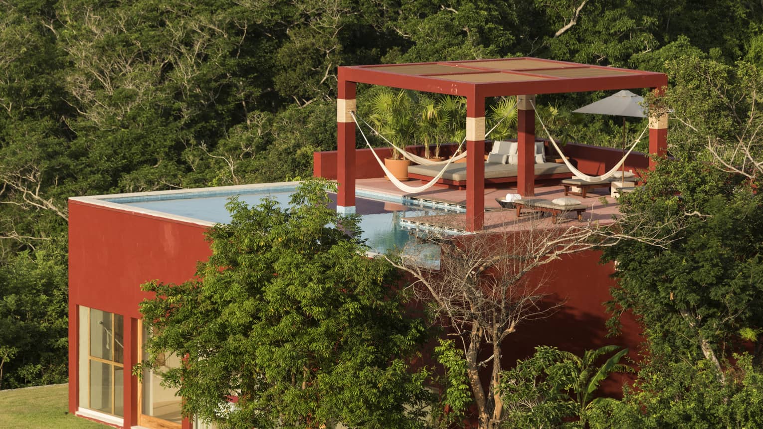 View of a red villa in the lush jungle forest with rooftop pool terrace