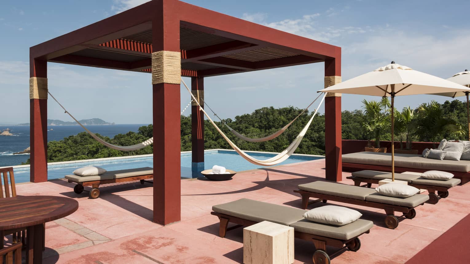 Pool terrace with lounge chairs and red pergola with hanging hammocks